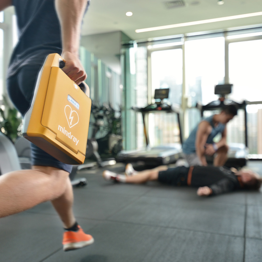 Person carrying Mindray BeneHeart C1A defibrillator to emergency in gym with collapsed patient
